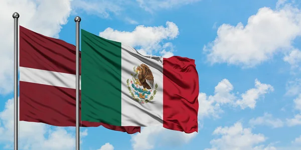 Bandera de Letonia y México ondeando en el viento contra el cielo azul nublado blanco juntos. Concepto diplomático, relaciones internacionales . — Foto de Stock