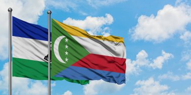 Lesotho ve Komor bayrağı birlikte beyaz bulutlu mavi gökyüzüne karşı rüzgarda sallayarak. Diplomasi kavramı, uluslararası ilişkiler.