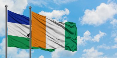 Lesotho ve Fildişi Sahili bayrağı birlikte beyaz bulutlu mavi gökyüzüne karşı rüzgarda sallayarak. Diplomasi kavramı, uluslararası ilişkiler.