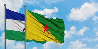 Lesotho ve Fransız Guyanası bayrağı birlikte beyaz bulutlu mavi gökyüzüne karşı rüzgarda sallayarak. Diplomasi kavramı, uluslararası ilişkiler.