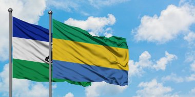 Lesotho ve Gabon bayrağı birlikte beyaz bulutlu mavi gökyüzüne karşı rüzgarda sallayarak. Diplomasi kavramı, uluslararası ilişkiler.