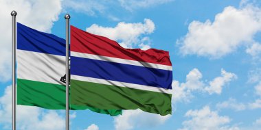 Lesotho ve Gambiya bayrağı birlikte beyaz bulutlu mavi gökyüzüne karşı rüzgarda sallayarak. Diplomasi kavramı, uluslararası ilişkiler.