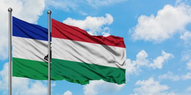 Lesotho ve Macaristan bayrağı birlikte beyaz bulutlu mavi gökyüzüne karşı rüzgarda sallayarak. Diplomasi kavramı, uluslararası ilişkiler.