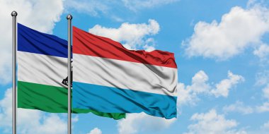 Lesotho ve Lüksemburg bayrağı birlikte beyaz bulutlu mavi gökyüzüne karşı rüzgarda sallayarak. Diplomasi kavramı, uluslararası ilişkiler.