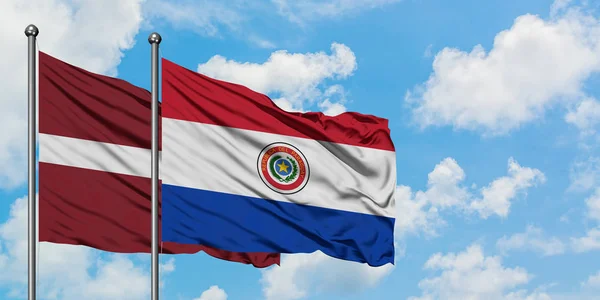 Lettonia e Paraguay bandiera sventolando nel vento contro bianco cielo blu nuvoloso insieme. Concetto di diplomazia, relazioni internazionali . — Foto Stock