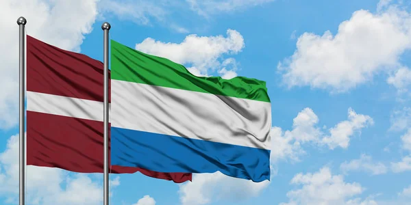 Lettonia e Sierra Leone sventolano insieme la bandiera contro il bianco cielo azzurro nuvoloso. Concetto di diplomazia, relazioni internazionali . — Foto Stock