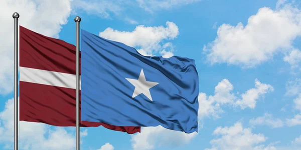 Łotwa i Somalia flaga machając w wiatr przed białym zachmurzone błękitne niebo razem. Koncepcja dyplomacji, stosunki międzynarodowe. — Zdjęcie stockowe