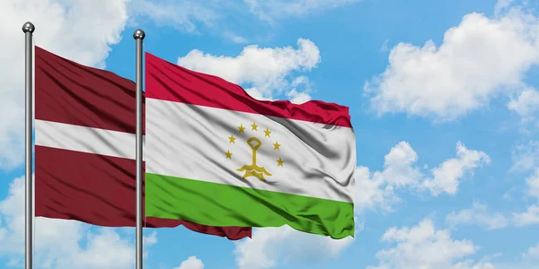 Bandera de Letonia y Tayikistán ondeando en el viento contra el cielo azul nublado blanco juntos. Concepto diplomático, relaciones internacionales . — Foto de Stock