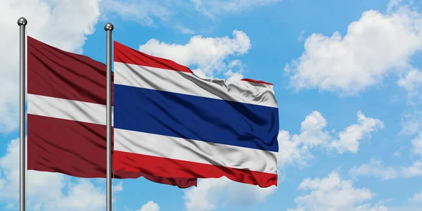 Bandera de Letonia y Tailandia ondeando en el viento contra el cielo azul nublado blanco juntos. Concepto diplomático, relaciones internacionales . — Foto de Stock