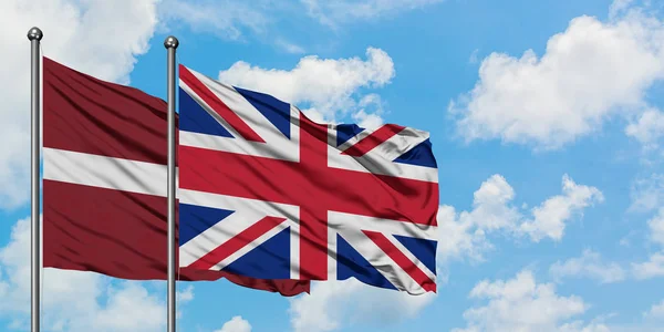 Lettland och Storbritannien flagga vifta i vinden mot vit grumlig blå himmel tillsammans. Diplomatisk koncept, internationella relationer. — Stockfoto