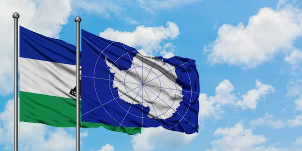 Lesotho och Antarktis flagga vinka i vinden mot vit grumlig blå himmel tillsammans. Diplomatisk koncept, internationella relationer. — Stockfoto
