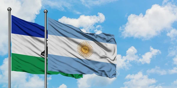 Lesoto e a bandeira da Argentina agitando no vento contra o céu azul nublado branco juntos. Conceito de diplomacia, relações internacionais . — Fotografia de Stock
