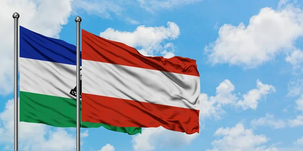 Lesotho és Ausztria zászló integetett a szél ellen, fehér felhős kék ég együtt. Diplomáciai koncepció, nemzetközi kapcsolatok. — Stock Fotó