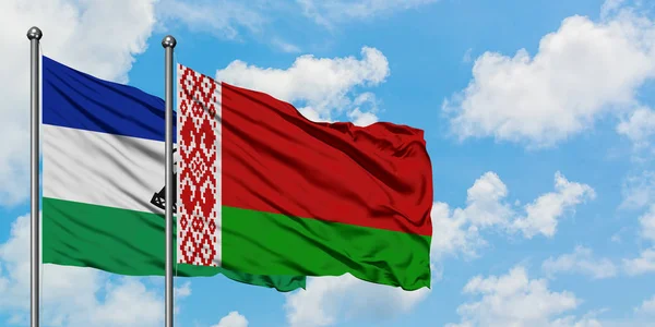 Lesotho y la bandera de Bielorrusia ondeando en el viento contra el cielo azul nublado blanco juntos. Concepto diplomático, relaciones internacionales . — Foto de Stock