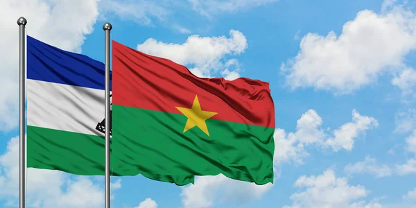 Bandera Lesotho y Burkina Faso ondeando en el viento contra el cielo azul nublado blanco juntos. Concepto diplomático, relaciones internacionales . — Foto de Stock