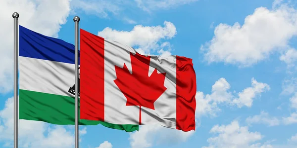 Lesotho y la bandera de Canadá ondeando en el viento contra el cielo azul nublado blanco juntos. Concepto diplomático, relaciones internacionales . — Foto de Stock