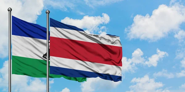 Bandera de Lesotho y Costa Rica ondeando en el viento contra el cielo azul nublado blanco juntos. Concepto diplomático, relaciones internacionales . — Foto de Stock