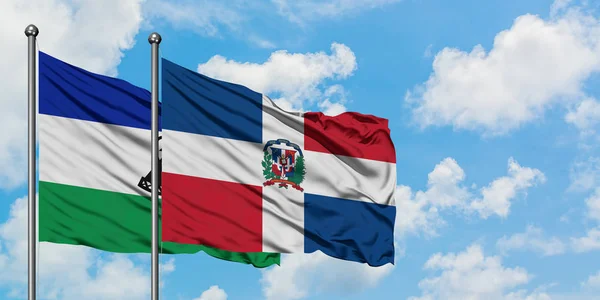 一緒に白い曇り青い空に対して風に手を振るレソトとドミニカ共和国の旗。外交概念、国際関係. — ストック写真