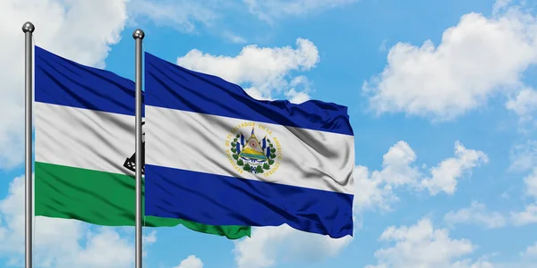 Bandera de Lesotho y El Salvador ondeando en el viento contra el cielo azul nublado blanco juntos. Concepto diplomático, relaciones internacionales . — Foto de Stock