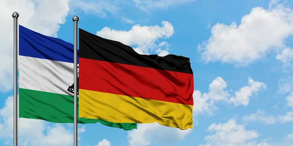 Lesotho y la bandera de Alemania ondeando en el viento contra el cielo azul nublado blanco juntos. Concepto diplomático, relaciones internacionales . — Foto de Stock