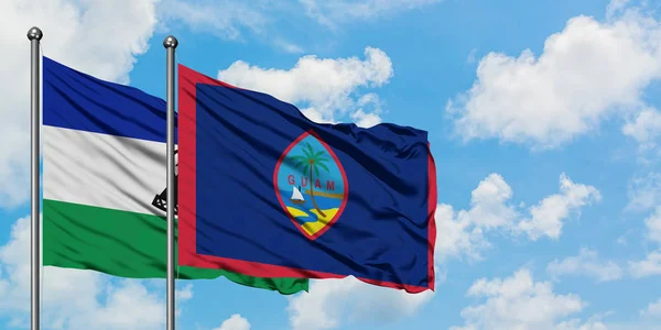 Bandera de Lesotho y Guam ondeando en el viento contra el cielo azul nublado blanco juntos. Concepto diplomático, relaciones internacionales . — Foto de Stock