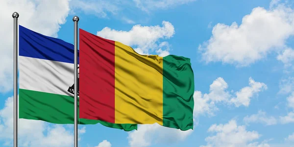 Lesotho e Guinea sventolano bandiera nel vento contro bianco cielo blu nuvoloso insieme. Concetto di diplomazia, relazioni internazionali . — Foto Stock
