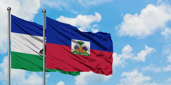 Lesotho y la bandera de Haití ondeando en el viento contra el cielo azul nublado blanco juntos. Concepto diplomático, relaciones internacionales . — Foto de Stock