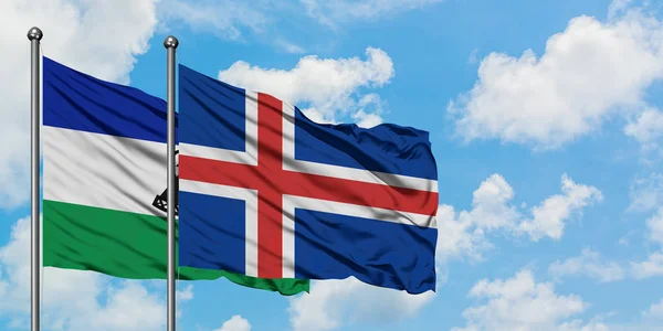 Lesotho y la bandera de Islandia ondeando en el viento contra el cielo azul nublado blanco juntos. Concepto diplomático, relaciones internacionales . — Foto de Stock