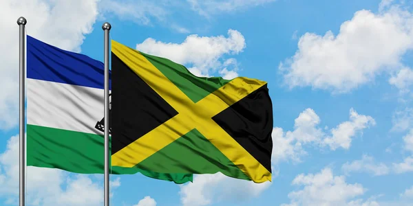 Lesotho y la bandera de Jamaica ondeando en el viento contra el cielo azul nublado blanco juntos. Concepto diplomático, relaciones internacionales . — Foto de Stock