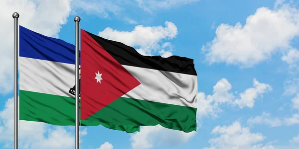 Lesotho y la bandera de Jordania ondeando en el viento contra el cielo azul nublado blanco juntos. Concepto diplomático, relaciones internacionales . — Foto de Stock