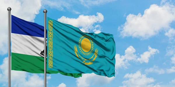 Lesotho y Kazajstán ondeando la bandera en el viento contra el cielo azul nublado blanco juntos. Concepto diplomático, relaciones internacionales . — Foto de Stock