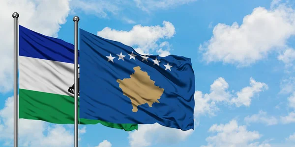 Lesotho y la bandera de Kosovo ondeando en el viento contra el cielo azul nublado blanco juntos. Concepto diplomático, relaciones internacionales . — Foto de Stock