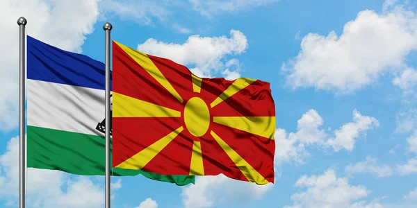 Bandera de Lesotho y Macedonia ondeando en el viento contra el cielo azul nublado blanco juntos. Concepto diplomático, relaciones internacionales . — Foto de Stock