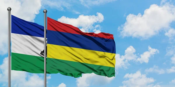 Lesotho e Mauritius sventolano nel vento contro il bianco cielo blu nuvoloso insieme. Concetto di diplomazia, relazioni internazionali . — Foto Stock