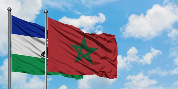 Lesotho y la bandera de Marruecos ondeando en el viento contra el cielo azul nublado blanco juntos. Concepto diplomático, relaciones internacionales . — Foto de Stock