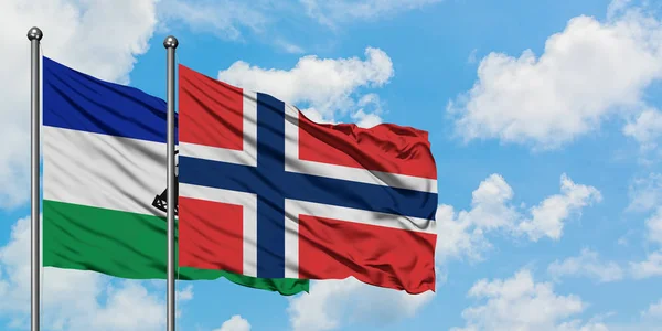 Lesotho y bandera de Noruega ondeando en el viento contra el cielo azul nublado blanco juntos. Concepto diplomático, relaciones internacionales . — Foto de Stock