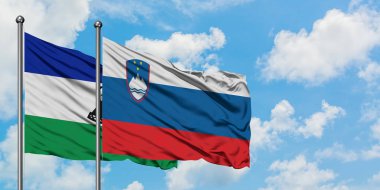 Lesotho ve Slovenya bayrağı birlikte beyaz bulutlu mavi gökyüzüne karşı rüzgarda sallayarak. Diplomasi kavramı, uluslararası ilişkiler.