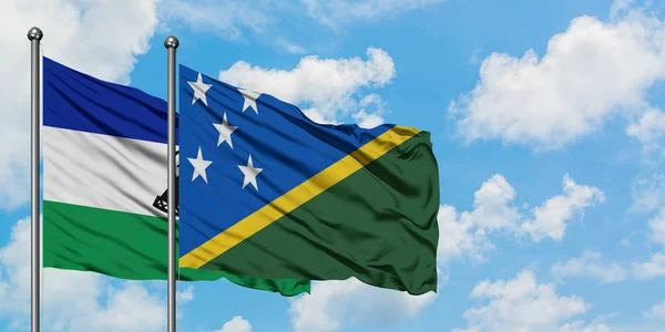 Lesotho y la bandera de las Islas Salomón ondeando en el viento contra el cielo azul nublado blanco juntos. Concepto diplomático, relaciones internacionales . — Foto de Stock