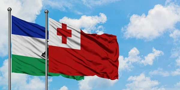 Lesotho y la bandera de Tonga ondeando en el viento contra el cielo azul nublado blanco juntos. Concepto diplomático, relaciones internacionales . — Foto de Stock
