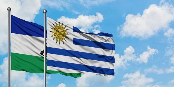 Lesotho und uruguay flagge wehen gemeinsam im wind vor weißem wolkenblauem himmel. Diplomatie-Konzept, internationale Beziehungen. — Stockfoto