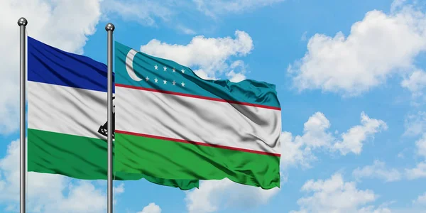 Lesotho e la bandiera dell'Uzbekistan sventolano nel vento contro il bianco cielo blu nuvoloso insieme. Concetto di diplomazia, relazioni internazionali . — Foto Stock