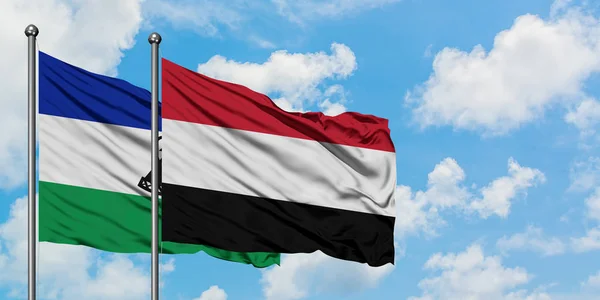 Bandera de Lesotho y Yemen ondeando en el viento contra el cielo azul nublado blanco juntos. Concepto diplomático, relaciones internacionales . — Foto de Stock