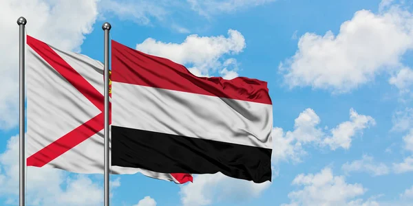 Jersey e Iêmen acenando com o vento contra o céu azul nublado branco juntos. Conceito de diplomacia, relações internacionais . — Fotografia de Stock