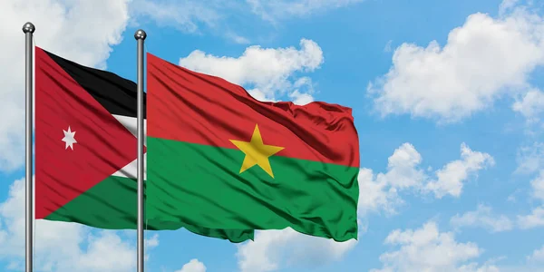 Bandera de Jordania y Burkina Faso ondeando en el viento contra el cielo azul nublado blanco juntos. Concepto diplomático, relaciones internacionales . — Foto de Stock