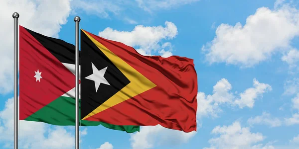 Bandera de Jordania y Timor Oriental ondeando en el viento contra el cielo azul nublado blanco juntos. Concepto diplomático, relaciones internacionales . — Foto de Stock