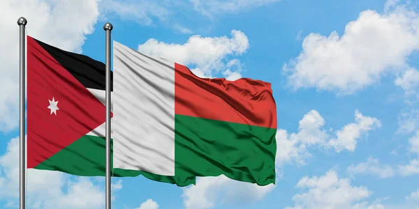 Bandera de Jordania y Madagascar ondeando en el viento contra el cielo azul nublado blanco juntos. Concepto diplomático, relaciones internacionales . — Foto de Stock