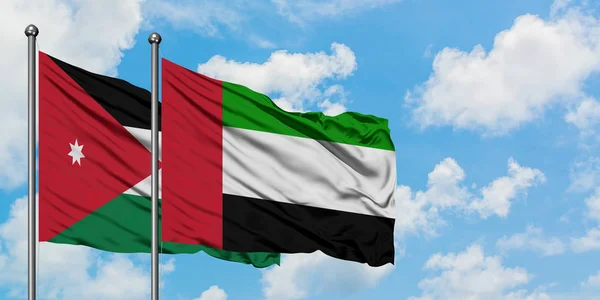Jordania y los Emiratos Árabes Unidos ondean en el viento contra el cielo azul nublado blanco juntos. Concepto diplomático, relaciones internacionales . — Foto de Stock