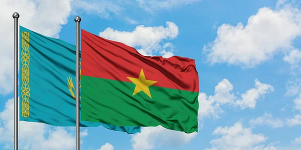 Bandera de Kazajstán y Burkina Faso ondeando en el viento contra el cielo azul nublado blanco juntos. Concepto diplomático, relaciones internacionales . — Foto de Stock