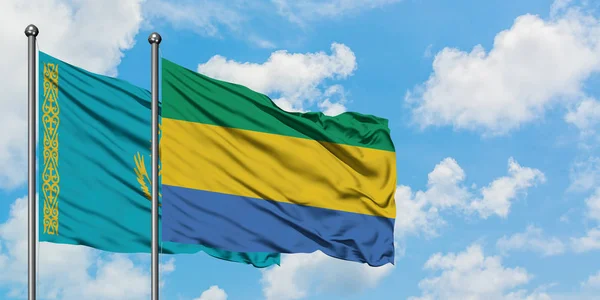 Drapeau du Kazakhstan et du Gabon agitant dans le vent contre ciel bleu nuageux blanc ensemble. Concept de diplomatie, relations internationales . — Photo