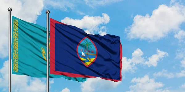 Bandera de Kazajstán y Guam ondeando en el viento contra el cielo azul nublado blanco juntos. Concepto diplomático, relaciones internacionales . — Foto de Stock